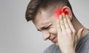 mężczyzna cierpiący na zapalenie nerwu przedsionkowo-ślimakowego trzyma się za bolące ucho