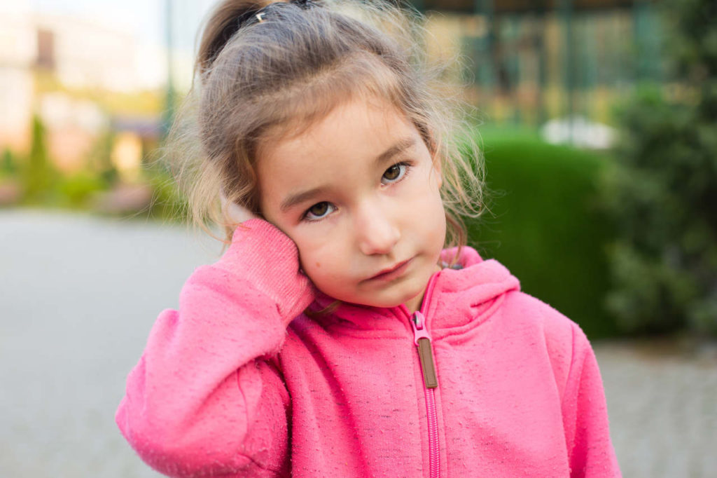 dziewczynka trzyma się za ucho, które boli ją z powodu zapalenia trąbki słuchowej